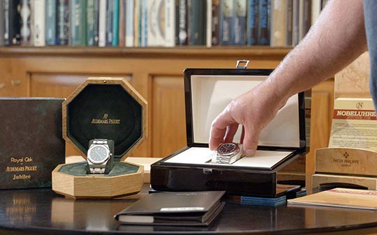 Foto von zwei Luxusuhren in der Original-Box. Eine Hand greift eine Uhr.